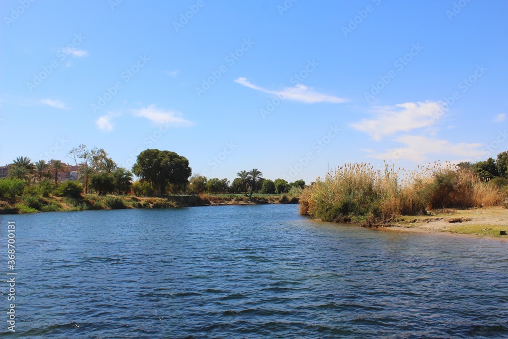 Calm Nile water with grass on river coast and blue sky in Egypt