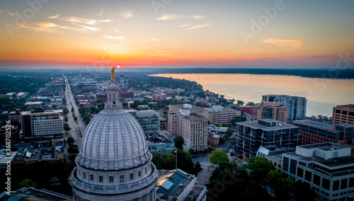 Wide aerial shot of a dramatic, fiery sunrise over the Wisconsin State Capitol. Statue atop the dome appears to hold the rising sun.