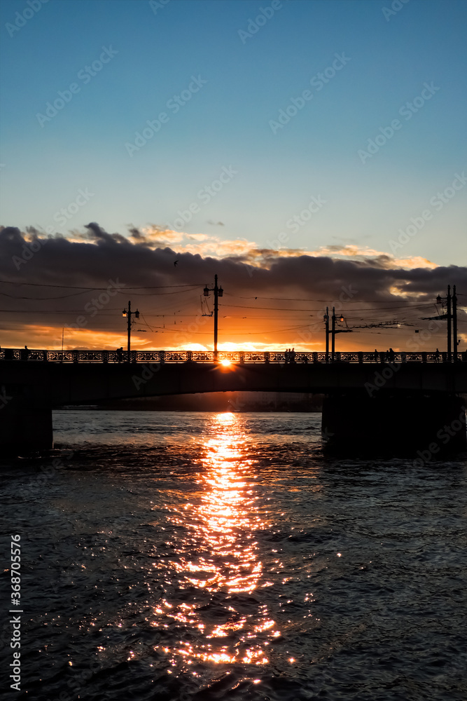 Urban night landscape. Bridge against the sunset. The glare of the sun on the water.  