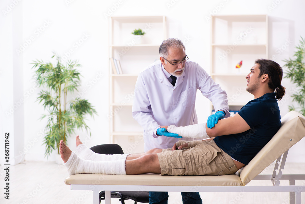 Young injured man visiting old doctor traumatologist Young injured man visiting old doctor traumatologist