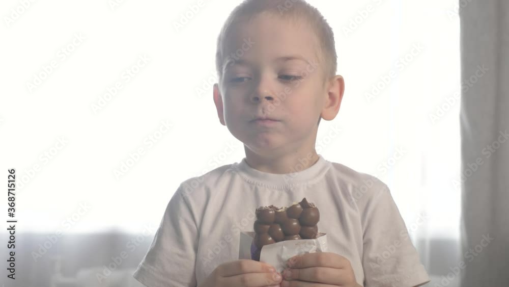 little boy eating chocolate. the child eats sweets. 5 year old blonde kid eating lifestyle chocolate bar indoors little boy eating chocolate. the child eats sweets. 5 year old blonde kid eating lifestyle chocolate bar indoors
