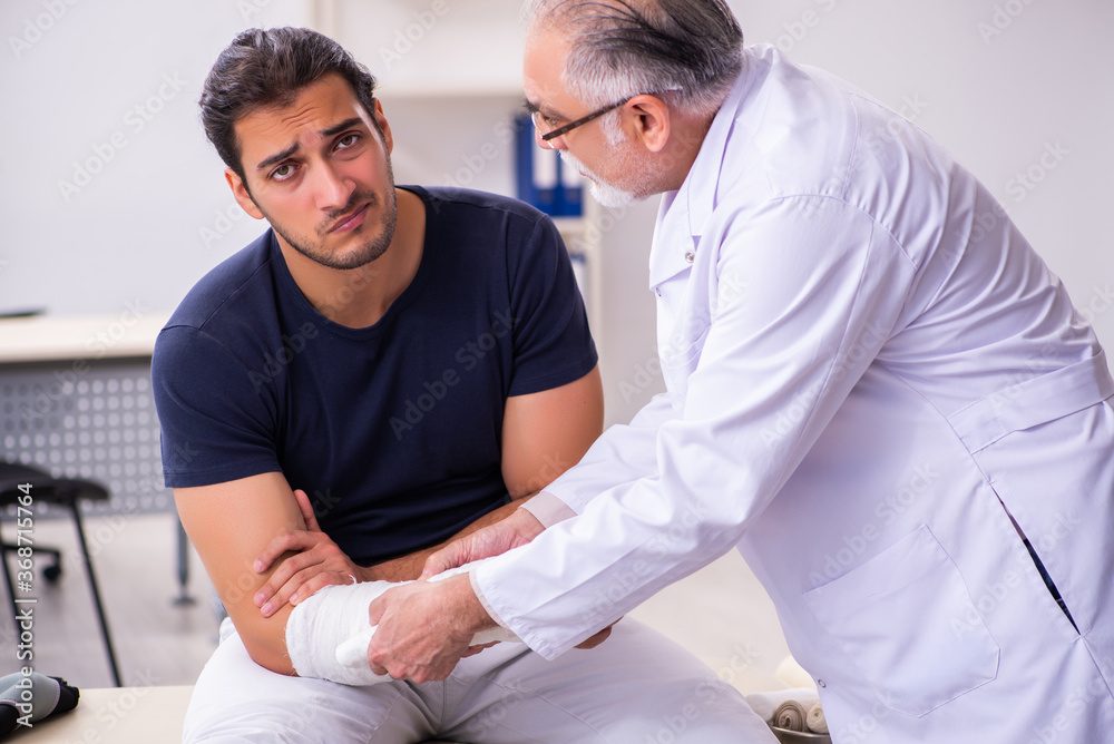 Obraz premium Young injured man visiting experienced male doctor traumatologis