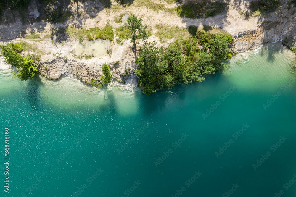 coastline of quarry lake with turquoise water and trees ashore. top view aerial photo