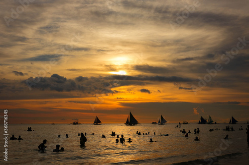 フィリピン・ボラカイ島のホワイトビーチにて、オレンジ色に輝く太陽が海に沈む夕焼けの空を眺める