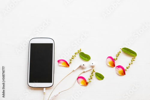 mobile phone ,earphone with petal coloful flowrers frangipani arrangement music score flat lay style on background white wooden photo