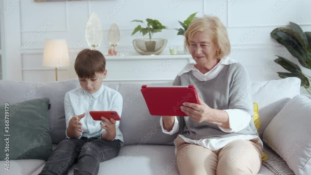 Gaming family. Excited old grandma and her adorable grandson enjoying time together exchanging mobile devices polaying online video games on social media. Gaming family. Excited old grandma and her adorable grandson enjoying time together exchanging mobile devices polaying online video games on social media.