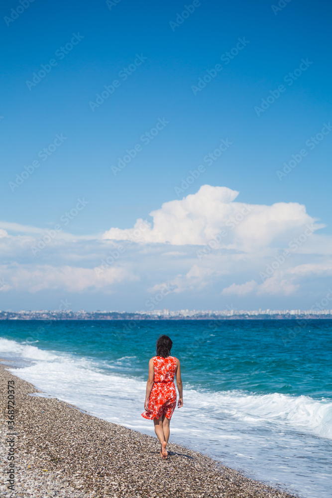 A girl in a dress walks along the beach and looks at the sea