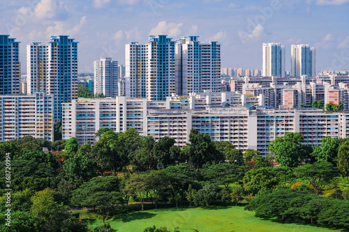 Architectural landscape of typical public housing HDB flats in blue and white on a bright sunny day, against lush park greenery in the foreground, Singapore. Beautiful day with blue sky and clouds