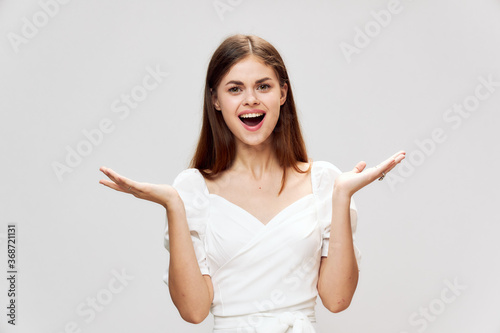 A cheerful woman with a wide open smile holds her hands in front of her white dress 