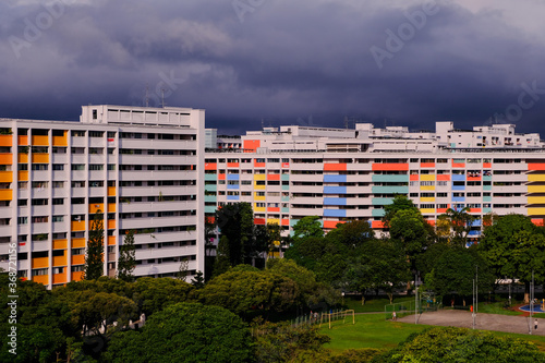 Dramatic dark grey clouds over common colourful HDB flats in Singapore neighbourhood heartland. Cheerful bright colourful of public housing architecture in yishun; lush greenery in front of flats
