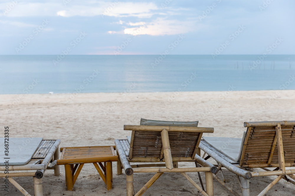 Bamboo deck chairs for tourists at peaceful beach under blue sky with calm sea morning light reflection as background. Picnic corner for visitors next to sandy beach Bamboo deck chairs for tourists at peaceful beach under blue sky with calm sea morning light reflection as background. Picnic corner for visitors next to sandy beach