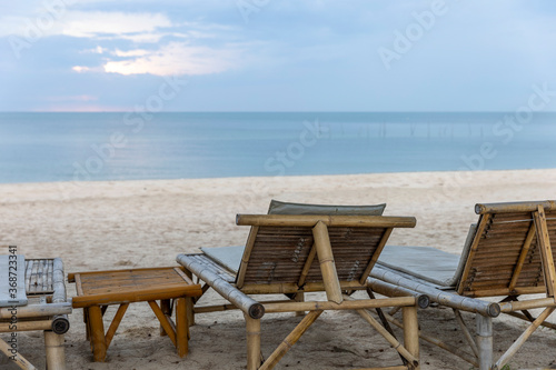 Bamboo deck chairs for tourists at peaceful beach under blue sky with calm sea morning light reflection as background. Picnic corner for visitors next to sandy beach