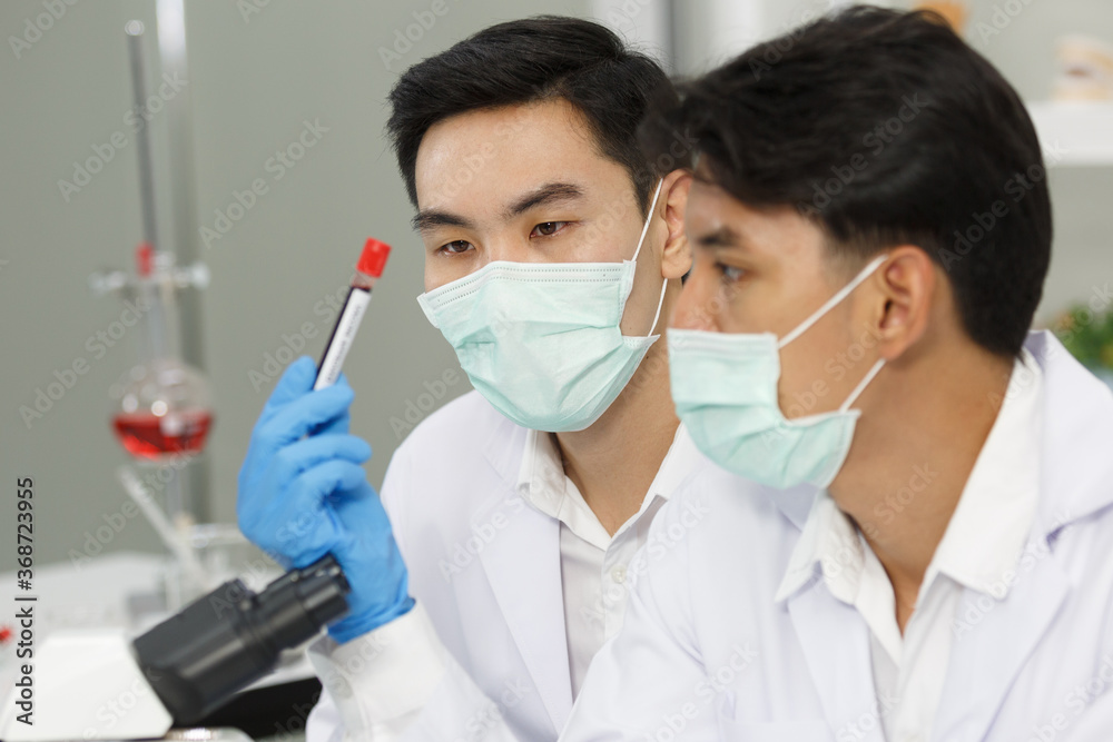 Two Male Scientists wear Face Mask working in Lab while Checking Blood tested by micro scope. SARS-CoV-2 , Covid-19 THEME. Two Male Scientists wear Face Mask working in Lab while Checking Blood tested by micro scope. SARS-CoV-2 , Covid-19 THEME.