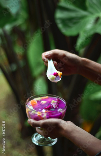 Portrait of a hand stirring Fruit soup. Fresh fruit soup mixed with syrup that is enjoyed in a green garden photo