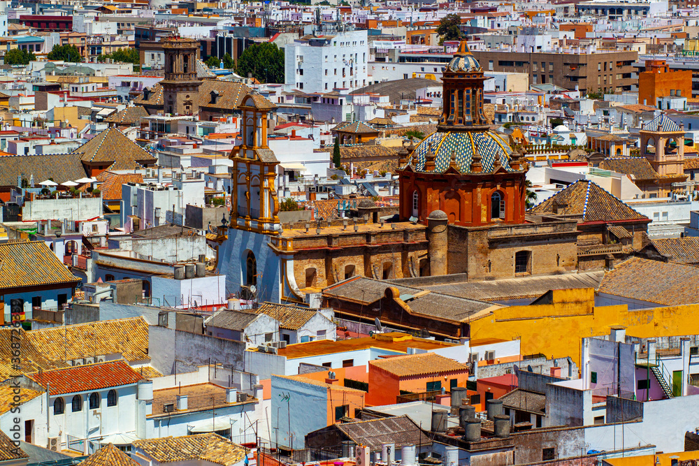 Aerial view of the historic district of Seville taken from the Giralda tower. Image features roof tops of vintage buildings and the decorative domed church Iglesia de Santa Cruz