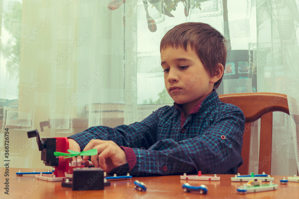 The boy playing an electric constructor. The child is played by intellectual toys. A boy in a blue shirt masters electronics. The concept of early development of children. toned The boy playing an electric constructor. The child is played by intellectual toys. A boy in a blue shirt masters electronics. The concept of early development of children. toned