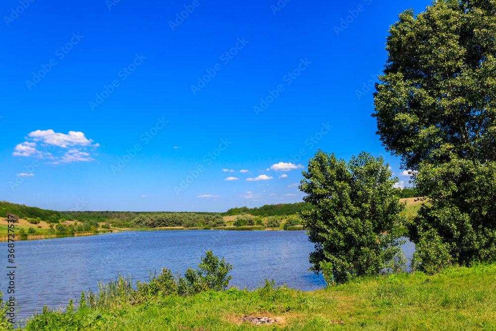 Obraz premium Summer landscape with beautiful lake, green meadows, hills, trees and blue sky