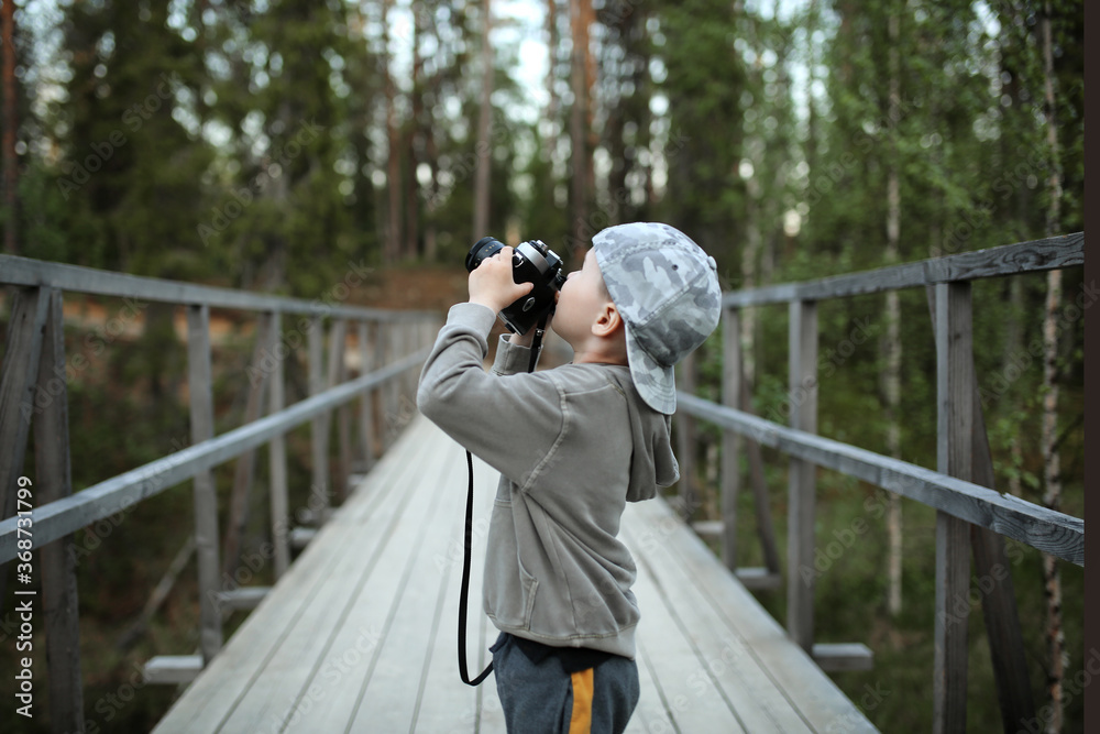young white boy in a cap is looking for an attractive and takes a photo with a camera against the background of a forest and outdoor recreation. Travel and leisure concept young white boy in a cap is looking for an attractive and takes a photo with a camera against the background of a forest and outdoor recreation. Travel and leisure concept