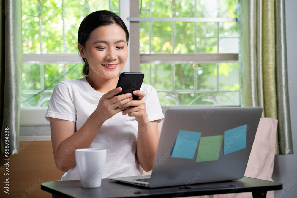 Asian woman happy typing message with smart phone sitting on the bed at home. WFH. Work from home.