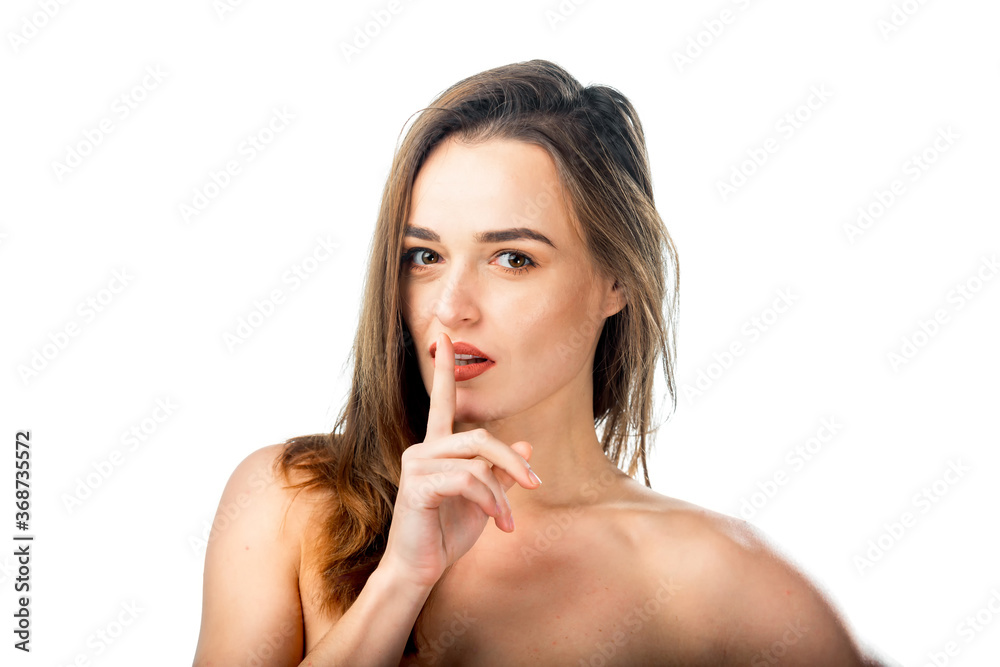Young female keeps finger near lips. Dark hair. Head and shoulders portrait. Poses against white background. Young female keeps finger near lips. Dark hair. Head and shoulders portrait. Poses against white background.