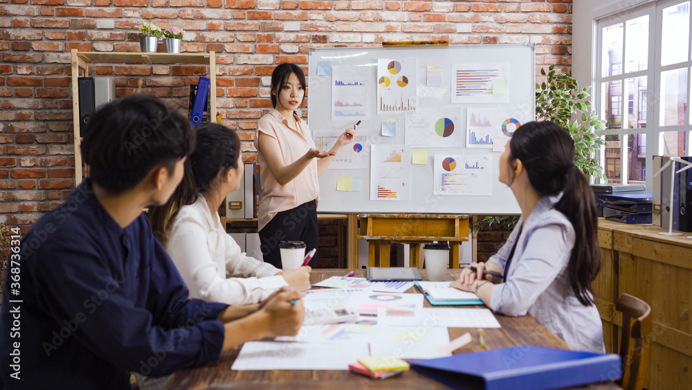 Fototapeta premium Female trainer invite willing worker come to flipchart present idea. asian man and women colleagues brainstorm at training show activity taking part in team building meeting. Cooperation concept