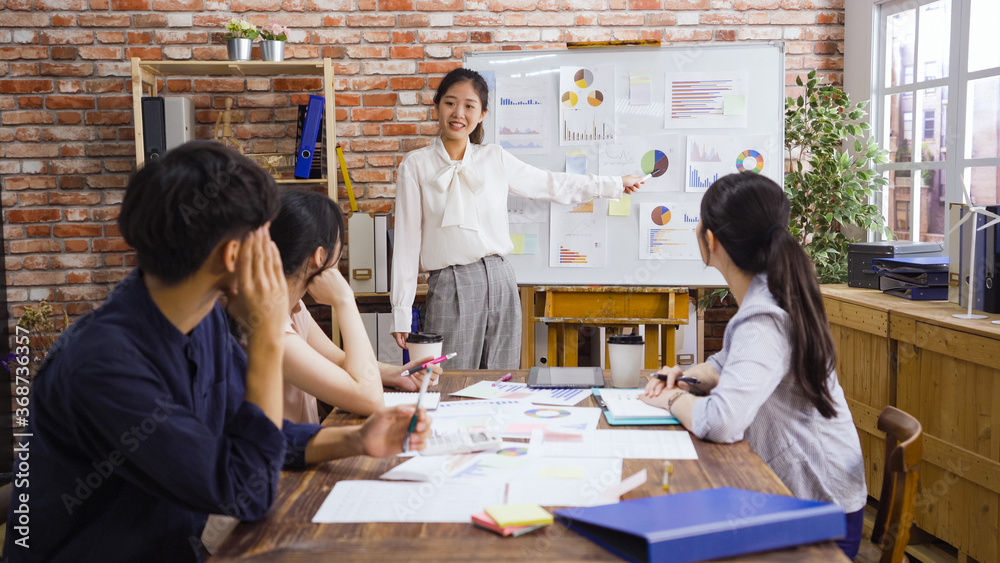 Fototapeta premium businesswoman at whiteboard giving presentation in modern boardroom. beautiful girl employee point at graph on flip chart and explaining opinion to male and female colleagues