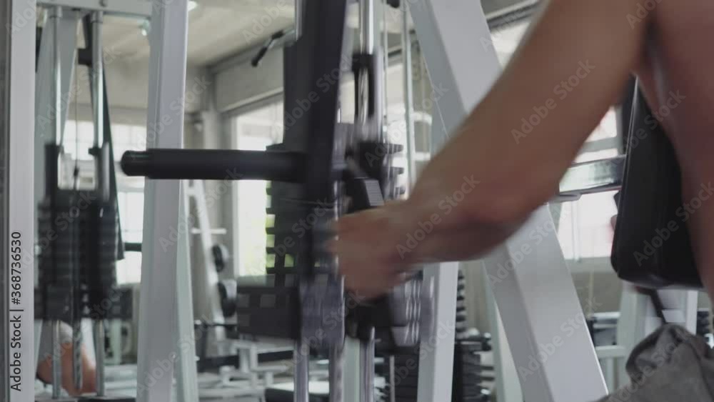 Medium shot : Side view of muscular man weight training exercise on seat back row machine. arm pull down for biceps and upper body bodybuilding. people workout lifestyle and healthy in fitness concept Medium shot : Side view of muscular man weight training exercise on seat back row machine. arm pull down for biceps and upper body bodybuilding. people workout lifestyle and healthy in fitness concept