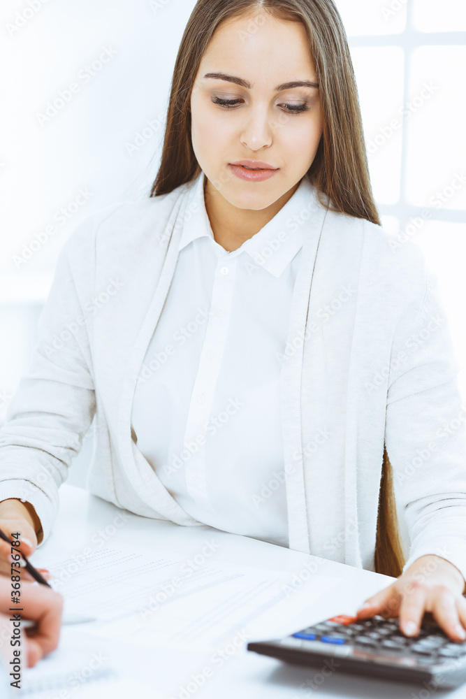 Young business woman and man sitting and working with computer and calculator in office. Bookkeeper checking balance or making finance report. Tax and audit concepts Young business woman and man sitting and working with computer and calculator in office. Bookkeeper checking balance or making finance report. Tax and audit concepts