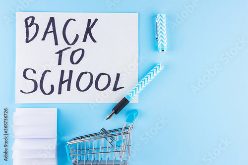 Back to school concept. Shopping cart and stationery on blue background. Pen, pencil and notepad for school. Top view