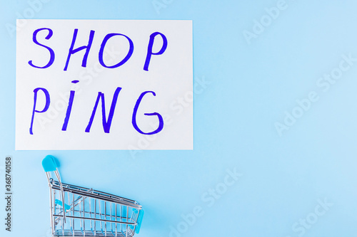 Shopping cart on blue background. Shop trolley at supermarket. Sale and discount. Consumer society trend. Concept of shopping. Copy space. Top view
