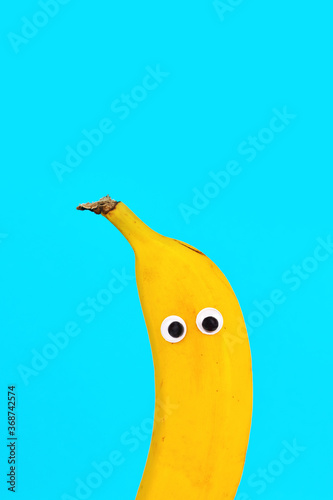 Funny Banana fruit with googly eyes on bright bue background with blank copy space above