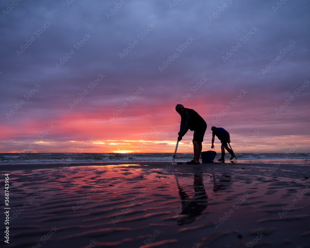 men on normandy beach during sunset look for worms to use as bait for fishing