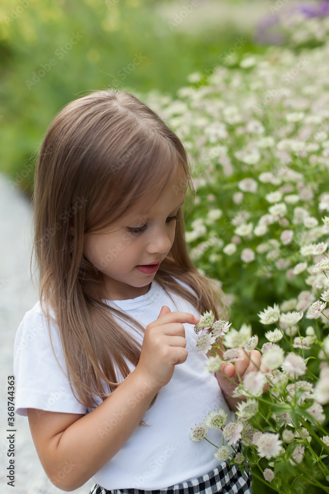 Little girl in the park on a summer day near a flower bed. The child gets lost on the street. Walking in the park. Little girl in the park on a summer day near a flower bed. The child gets lost on the street. Walking in the park.