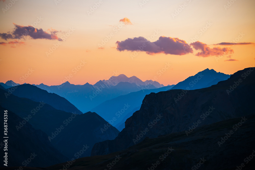 Colorful dawn landscape with beautiful mountains silhouettes and golden gradient sky with lilac clouds. Vivid mountain scenery with picturesque multicolor sunset. Scenic sunrise view to mountain range