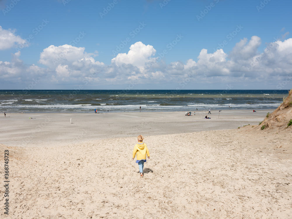The coast of the island of Ameland in The Netherlands. A young girls walks towards the ocean. The coast of the island of Ameland in The Netherlands. A young girls walks towards the ocean.