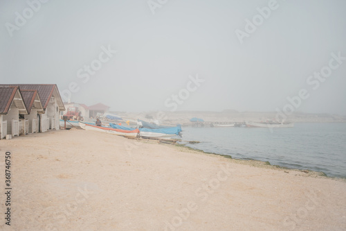 Minimal seascape on a foggy morning with fisherman and fishing boats by the sea shore. Modern and simple seaside landscape. Zen mind, peaceful activities by the sea, mindfulness concept.  © Andra
