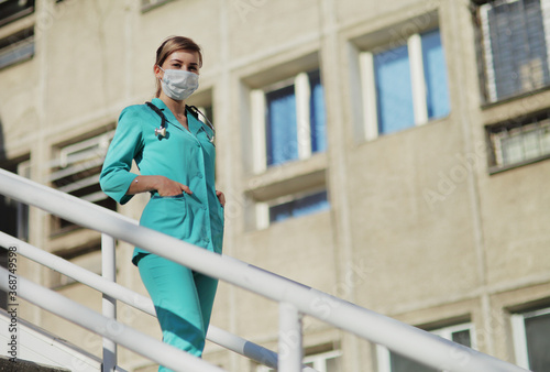 Female doctor or nurse in a protective face mask walking up the stairs © Maksim Selin