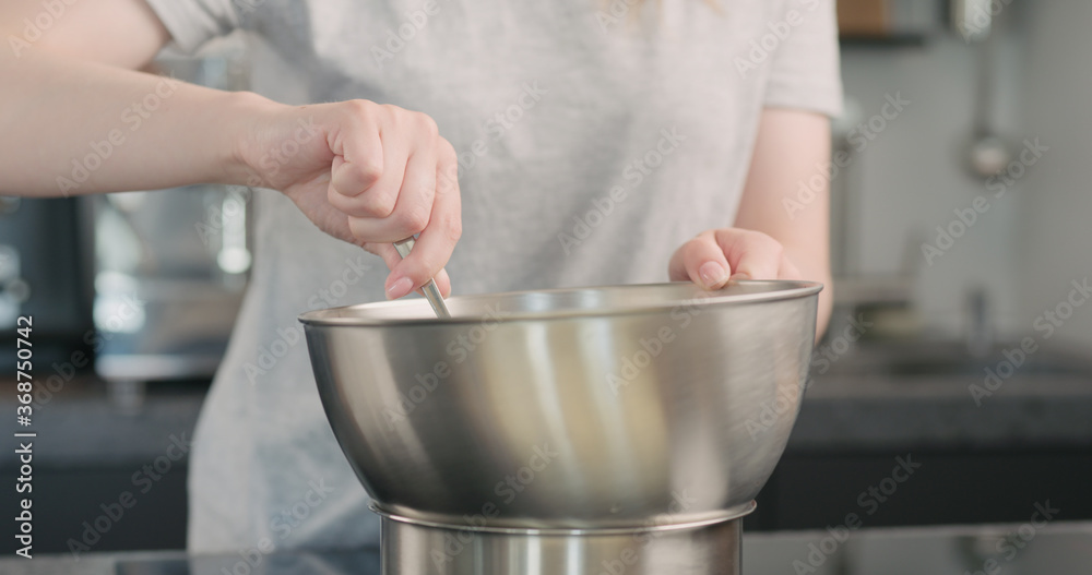 young woman mxing melted chocolate in stainless steel bowl on kitchen