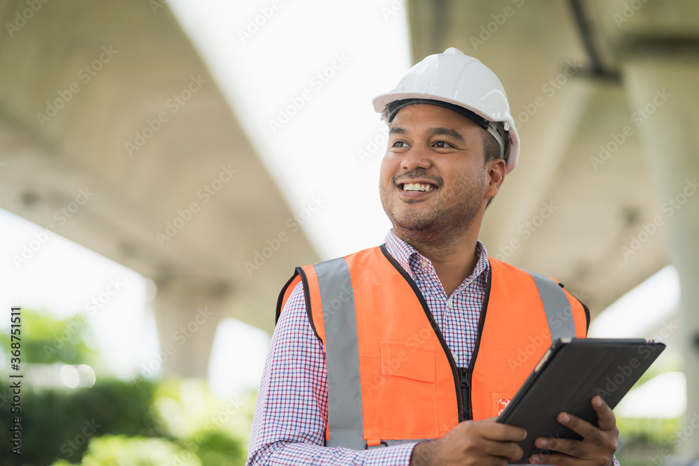 Asian civil engineer operate with tablet to control working at construction. Worker wearing hard hat at highway concrete road site. - obrazy, fototapety, plakaty 