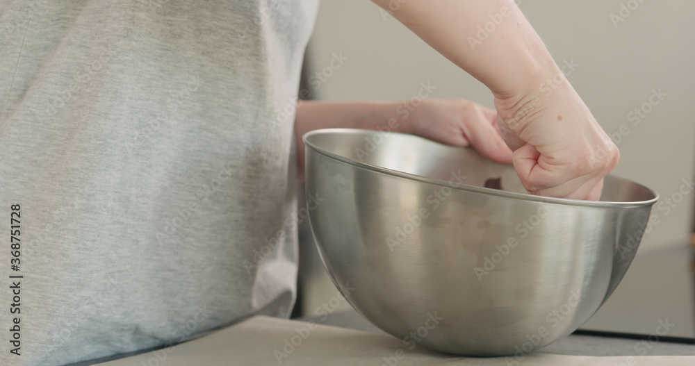 young woman mxing melted chocolate in stainless steel bowl on kitchen