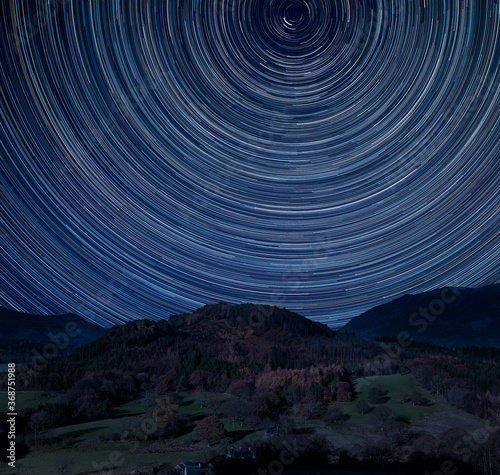 Digital composite image of star trails around Polaris with Stunning vibrant Catbells near Derwentwater in the Lake District with vivid Fall colors all around the contryside scene