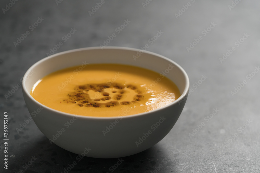 Pumpkin soup decorated with herbs and olive oil in white bowl on concrete background with copy space