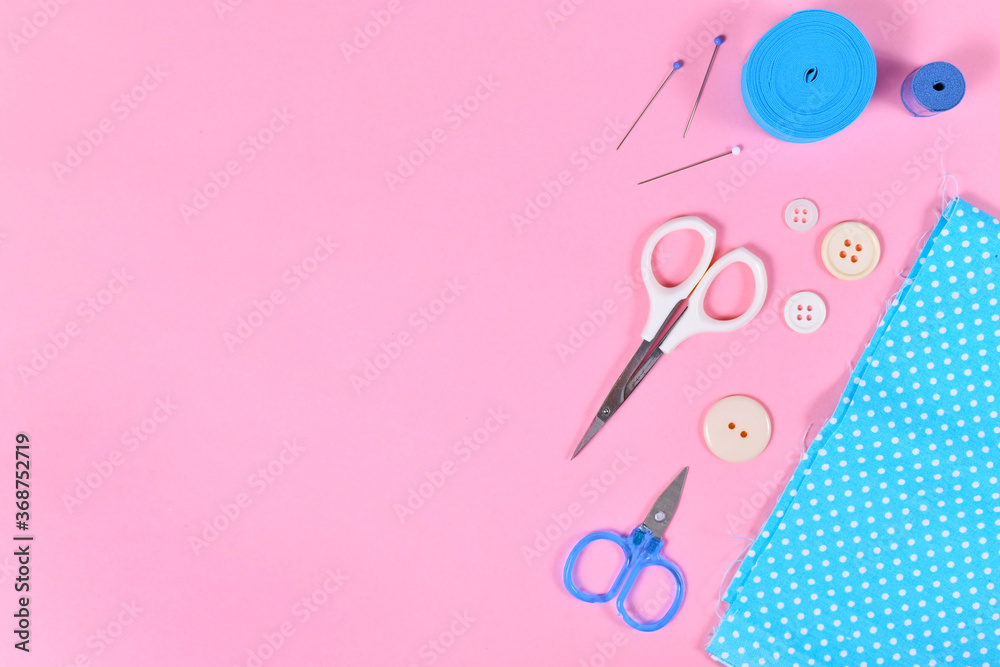 Flat lay with various sewing tools like fabric, scissors, buttons or pins on pink background with blank copy space on left side Flat lay with various sewing tools like fabric, scissors, buttons or pins on pink background with blank copy space on left side