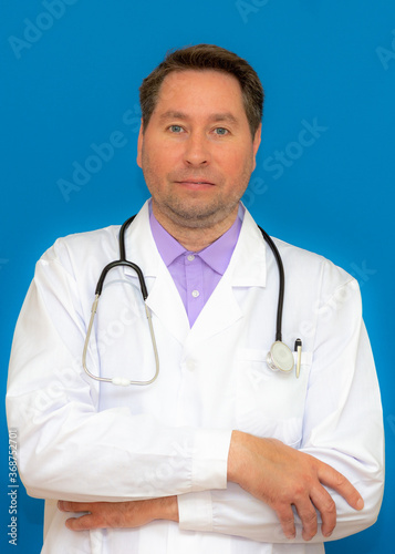 vertical Photo of caucasian brunet hair bristle doc assistant folded hands over chest stand on blue background