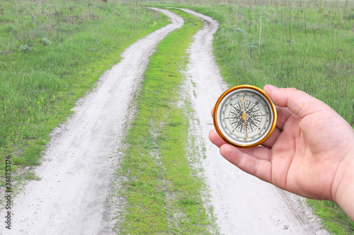 Old classic navigation compass in hand on background of road as symbol of tourism with compass, travel with compass and outdoor activities with compass