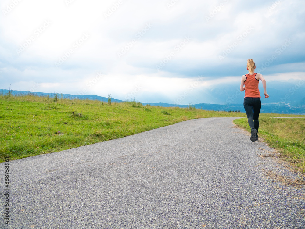 Young woman runner running seen from behind on the hill in nature with cloudy sky