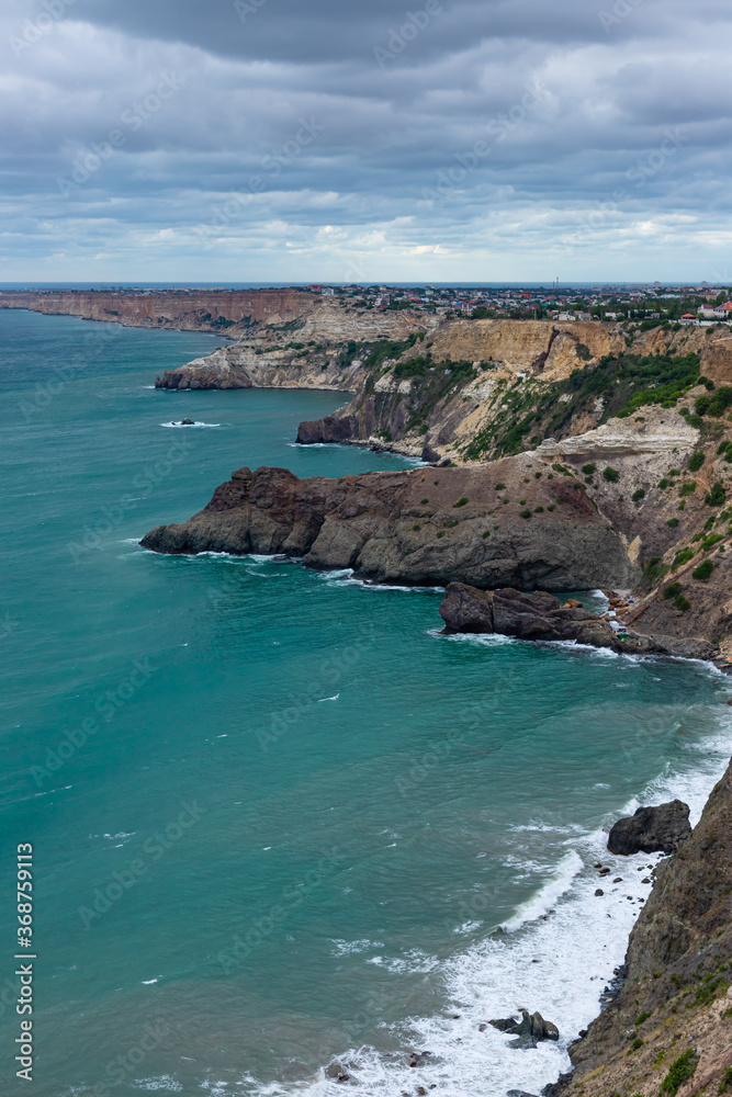 Calm azure sea and rocky seashore. View of the Black Sea coast in Crimea, Cape Fiolent, Russia. Vertical image