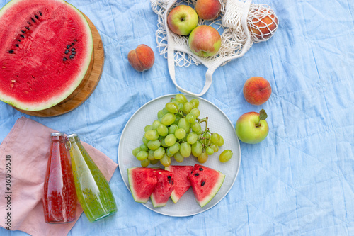 Fototapeta Naklejka Na Ścianę i Meble -  Summer picnic setting with a variety of delicious fruits, watermelon and refreshing drinks on a blue blanket. Beautiful lifestyle concept. Top view. copy space.