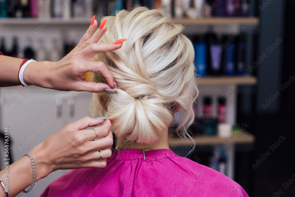 Fototapeta premium hairdresser makes his own hands hairstyle a bun on the head of a blonde girl