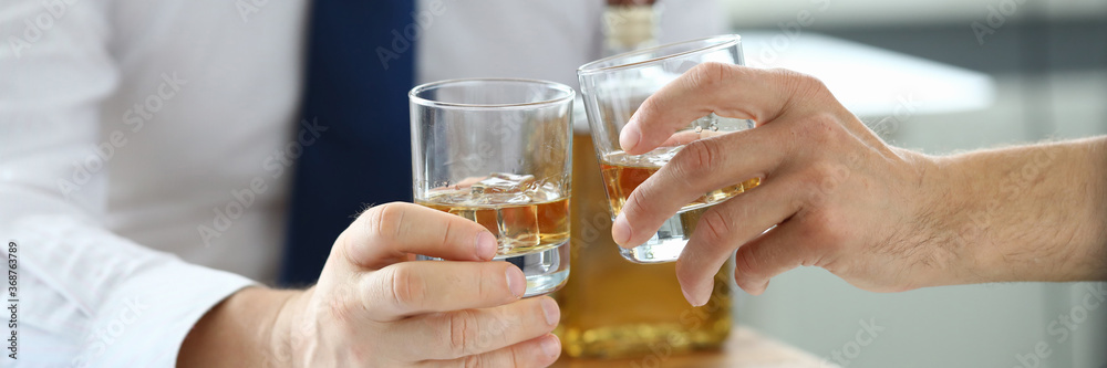Close-up of office workers clink glasses after making good deal. Partners celebrating signing important agreement with cognac. Papers and documents on table. Business concept Close-up of office workers clink glasses after making good deal. Partners celebrating signing important agreement with cognac. Papers and documents on table. Business concept